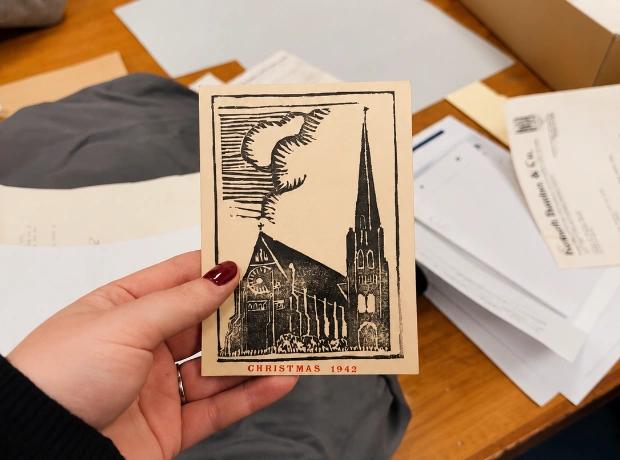 A researcher holding a vintage 1942 Christmas card showing a church illustration during archival cataloguing.