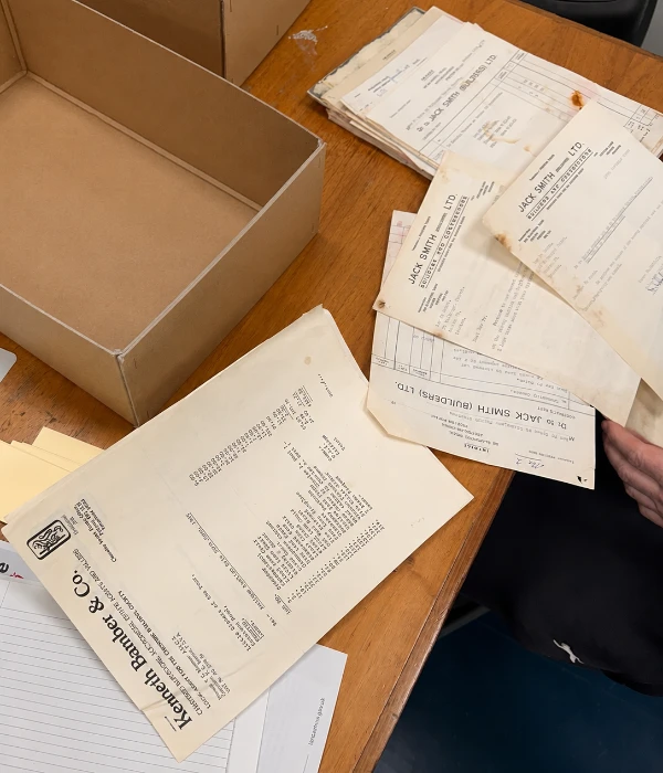 Open archive boxes and historic documents spread across a table while volunteers sort through paperwork in preparation for cataloguing.