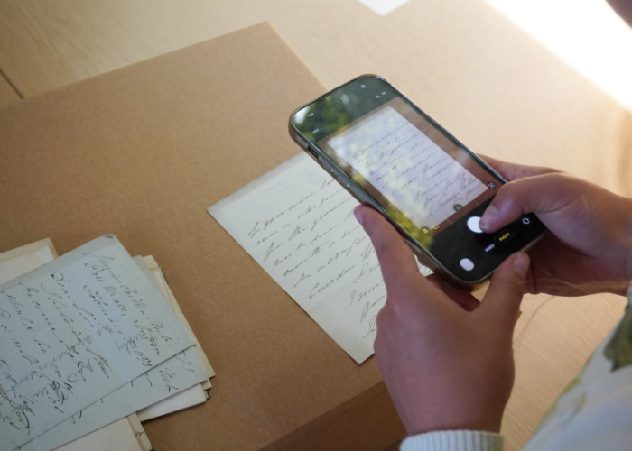 Close-up view of a person using a smartphone camera to digitise a historic handwritten letter resting on an archival box.