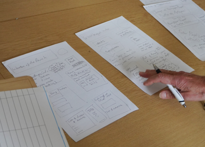 A person's hand pointing a pen at hand-drawn storyboards and mock-ups layout sheets for an exhibition on St Walburge's history.