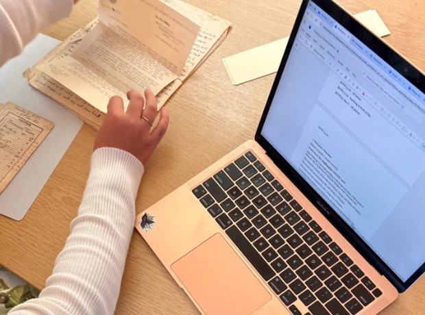 Overhead view of a researcher sorting through vintage archival documents next to a laptop displaying St Walburge's exhibition planning notes.