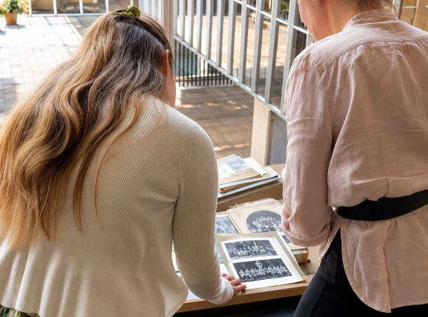 Over-the-shoulder view of two women standing by a desk to look through historic black-and-white group photographs at the Lancashire County Council offices.