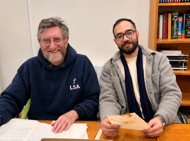 Two volunteers sitting at a table with archive documents, smiling at the camera.
