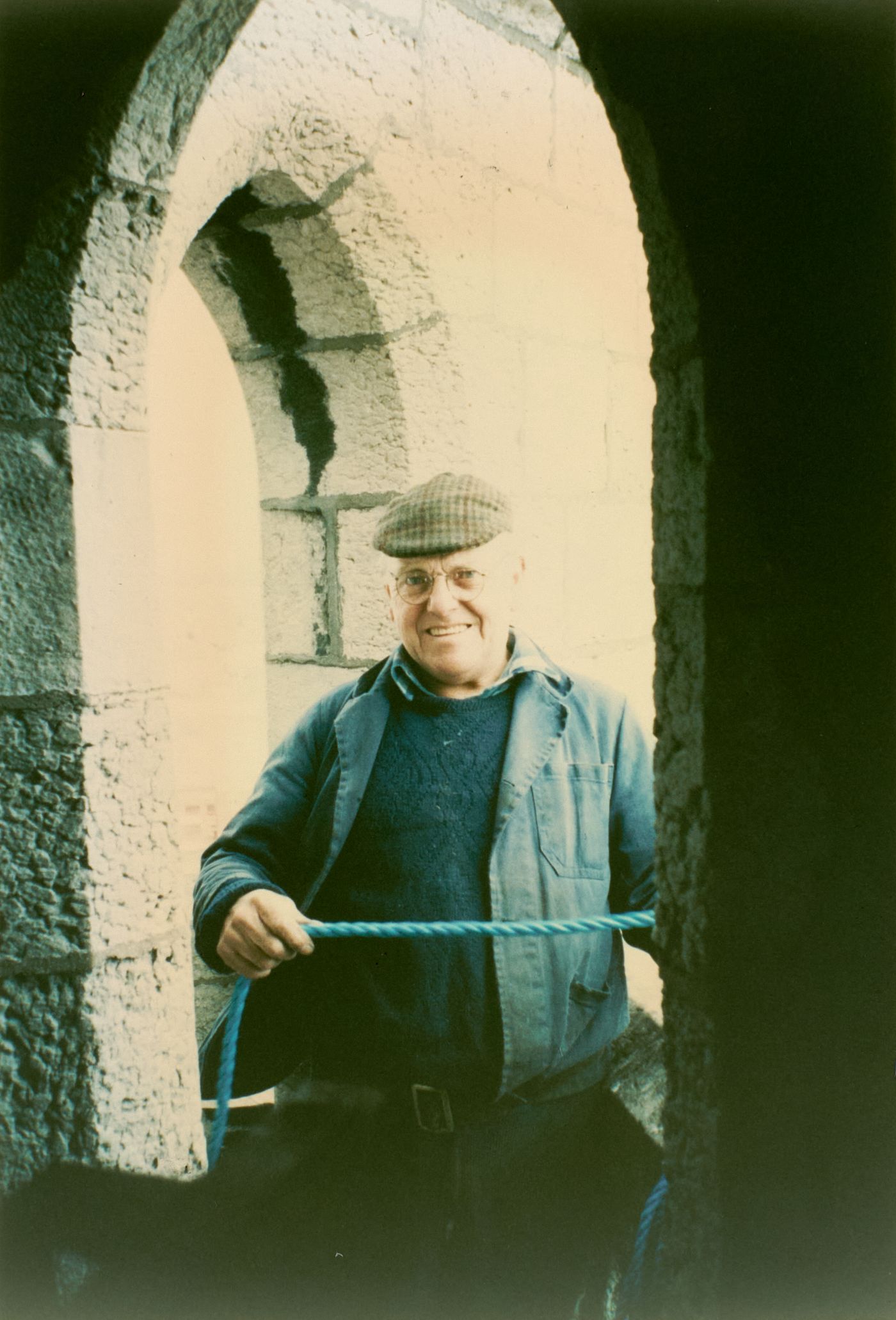Photograph of famous steeplejack and TV personality Fred Dibnah, smiling, holding a blue rope, standing in a stone archway high on St Walburge's.