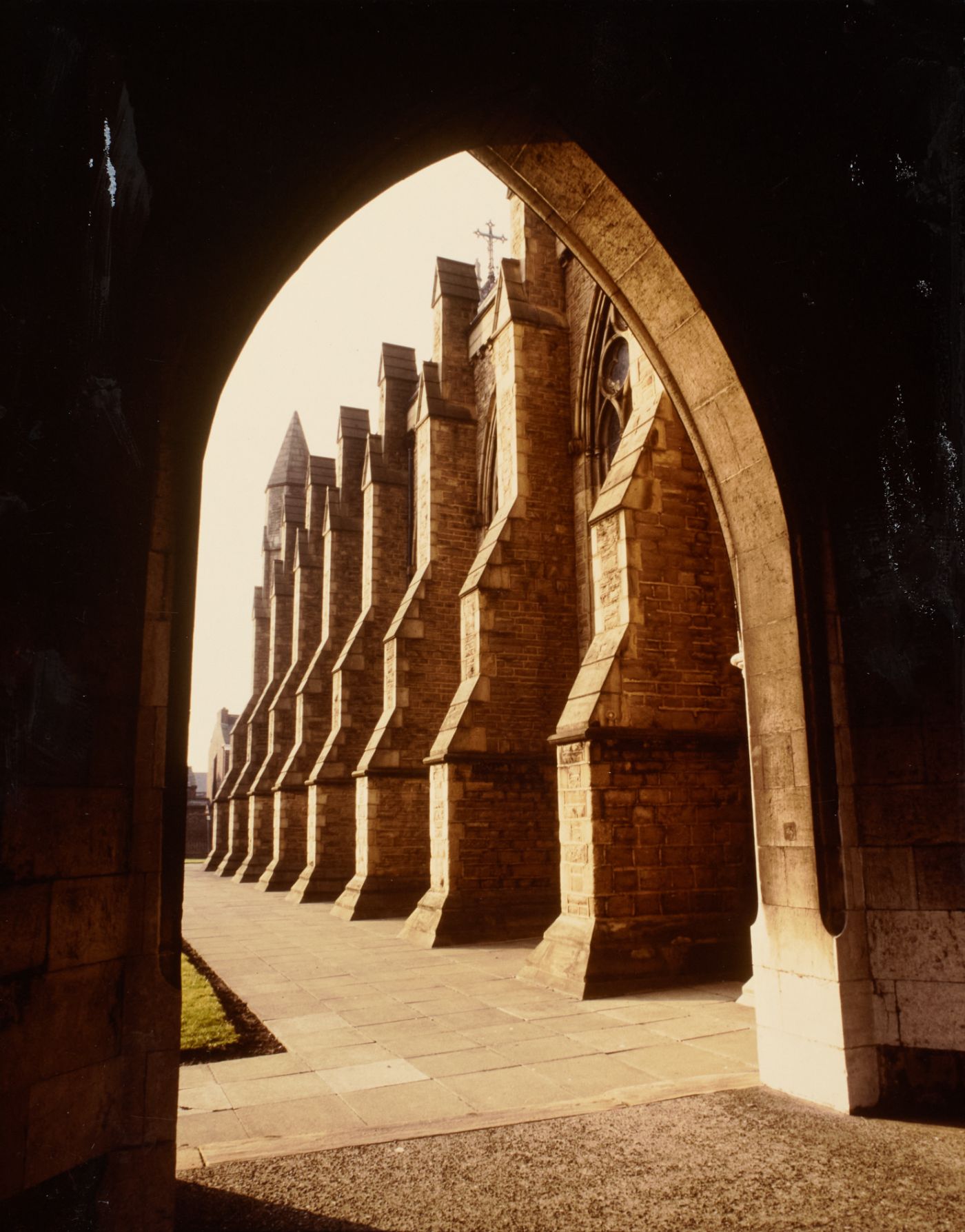 Photograph of St Walburge's south wall and stepped buttresses, seen in receding line through the stone arch of the porch.