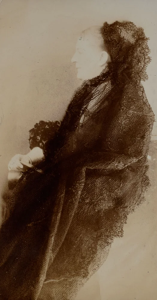 Faded, old photograph in profile of an elderly woman wrapped in a black lace shawl draped over her head and shoulders.