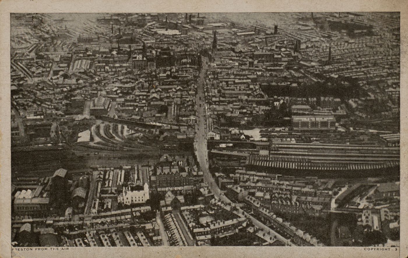 Printed postcard of Preston seen from the air, dense terraced streets and a railway station and sidings running across the middle distance, captioned "Preston from the Air."