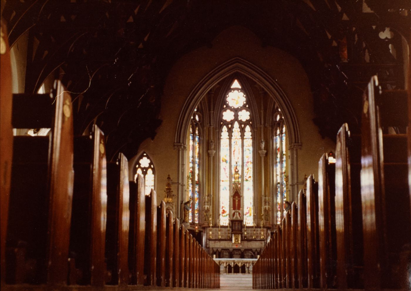 Colour photograph looking down the empty nave of St Walburge's toward the sanctuary, dark wooden pews leading the eye to the great east window and altar.