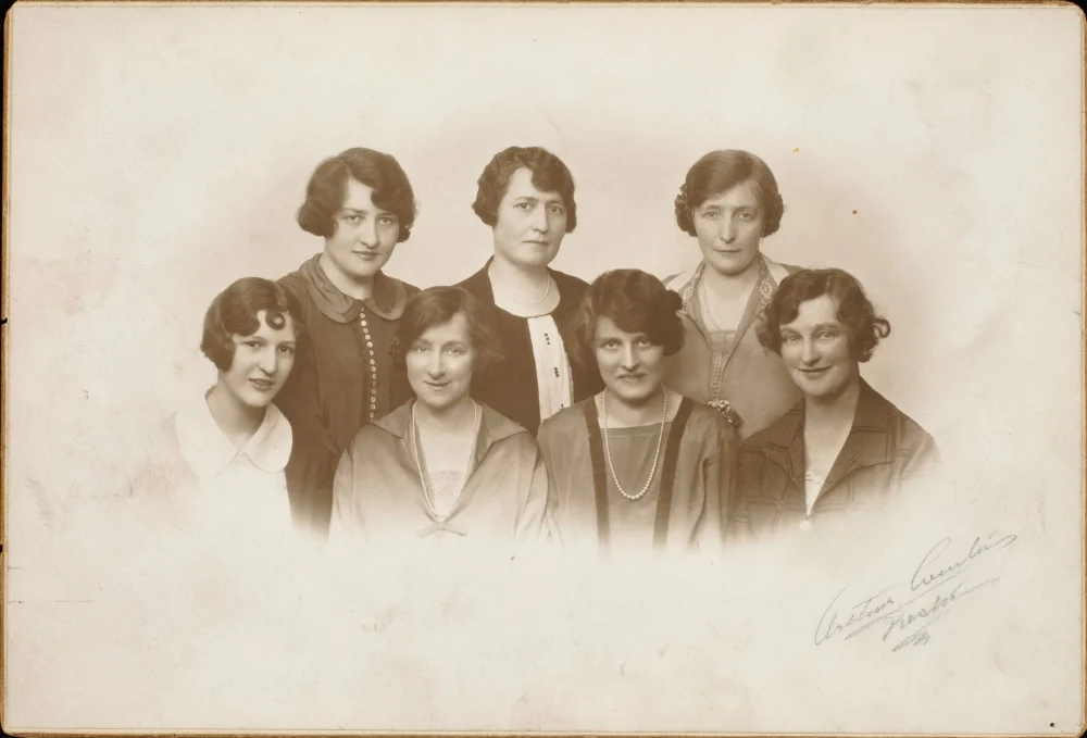 Sepia studio portrait of seven women in two rows, photographer's signature in the bottom corner reading "Arthur Curtis, Preston."