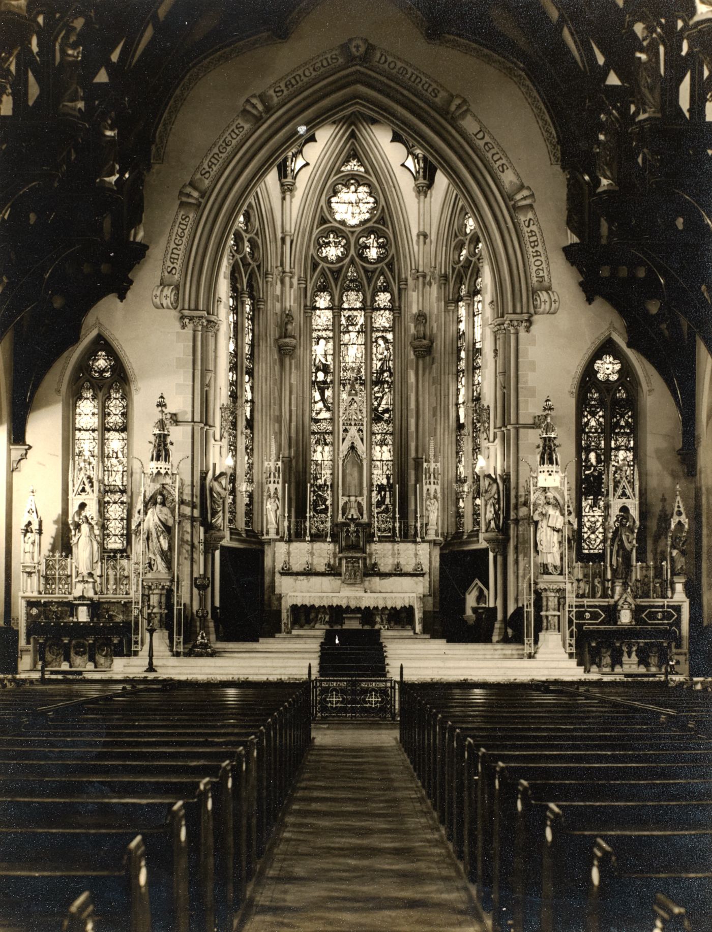 Photograph of St Walburge's sanctuary and great east window seen down the empty nave, side altars either side, pews in the foreground.