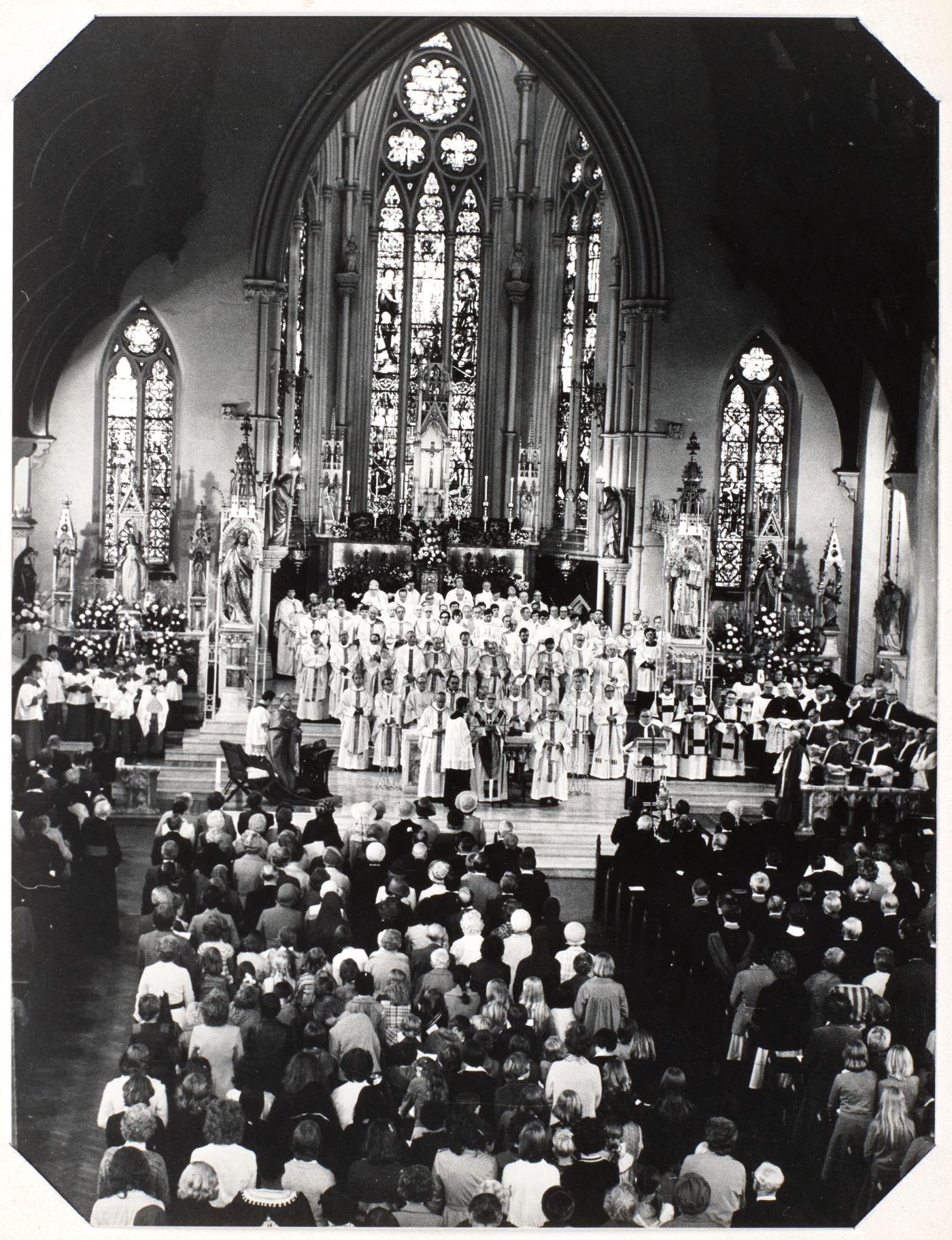 Photograph of Mass at St Walburge's, many priests in white vestments filling the sanctuary before the great east window, a full congregation standing at the pews.