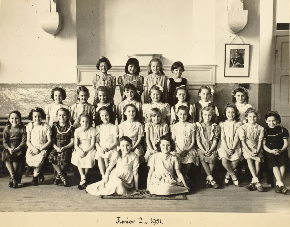 Girls of Junior 2 gather indoors in tiered rows for a class photograph, captioned "Junior 2 – 1951."