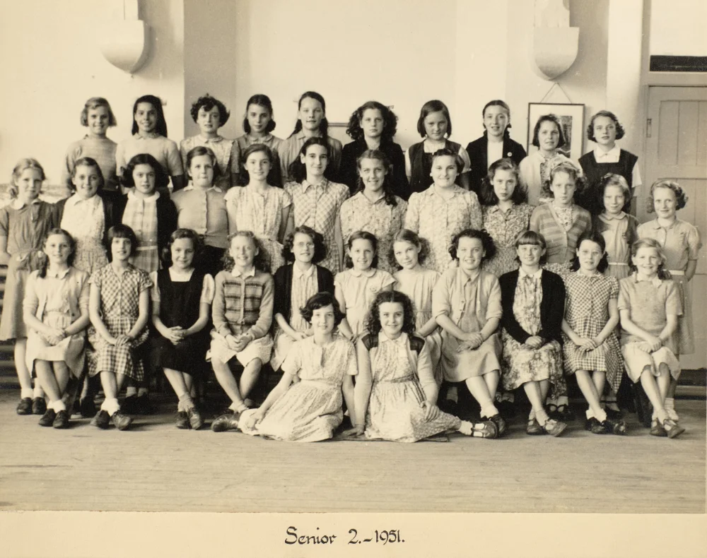 Girls of Senior 2 gather indoors in tiered rows for a class photograph, captioned "Senior 2 – 1951."