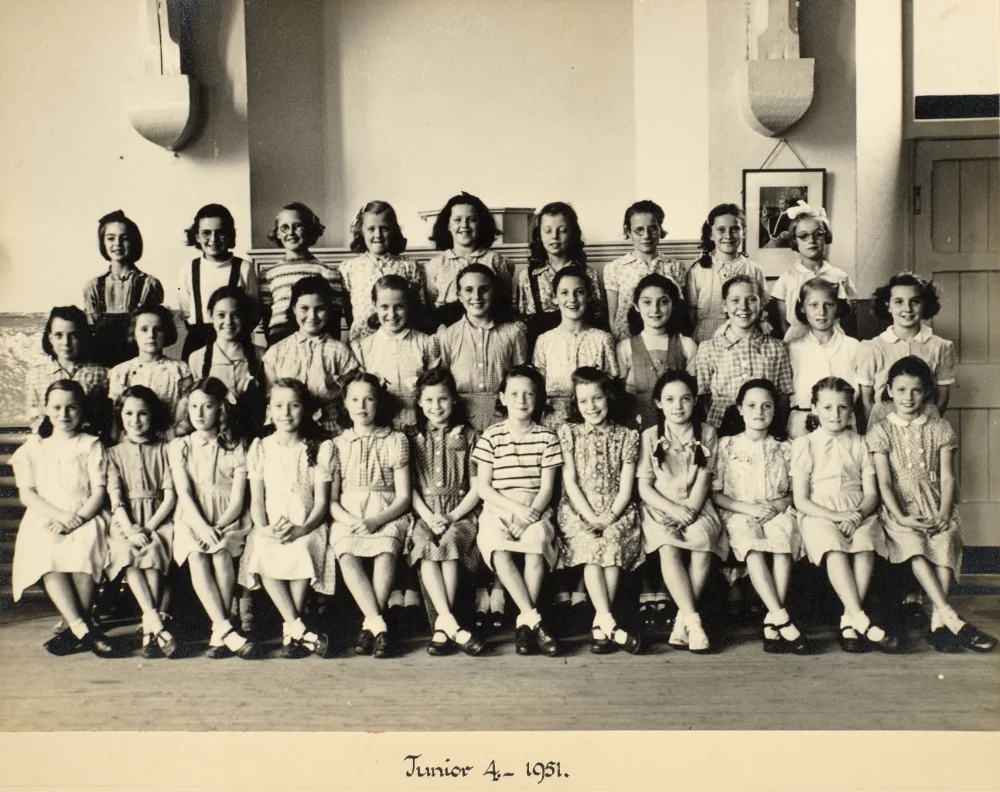 Girls of Junior 4 gather indoors in tiered rows for a class photograph, captioned "Junior 4 – 1951."