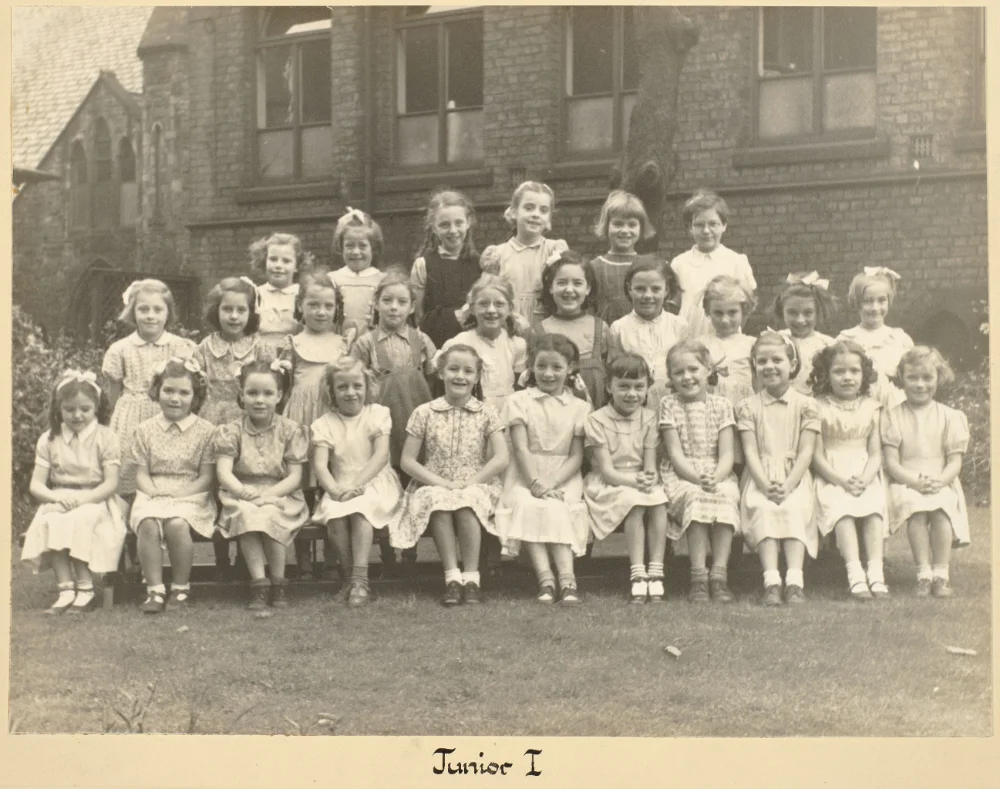 Girls of Junior 1 gather on the grass in tiered rows for a class photograph, captioned "Junior 1."
