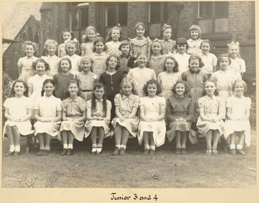 Girls of Junior 3 and 4 gather on the grass in tiered rows for a combined class photograph, captioned "Junior 3 and 4."