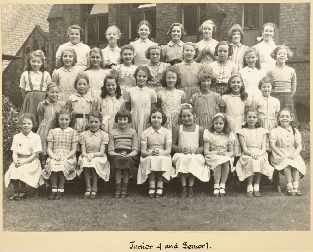 Girls of Junior 4 and Senior 1 gather on the grass in tiered rows for a combined class photograph, captioned "Junior 4 and Senior 1."