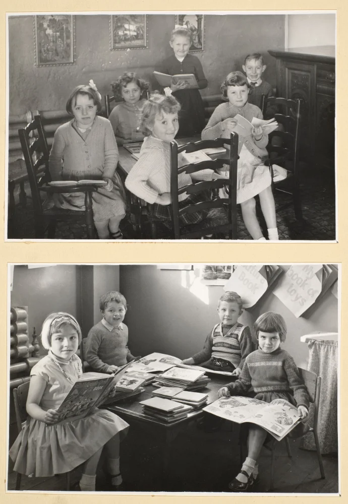 Infant pupils sit reading picture books at tables; a teacher stands reading in the upper photograph, framed pictures on the wall behind.