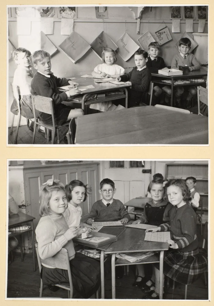 Infant pupils sit at classroom tables with paper and cards, work sheets pinned to the wall above in the upper photograph.