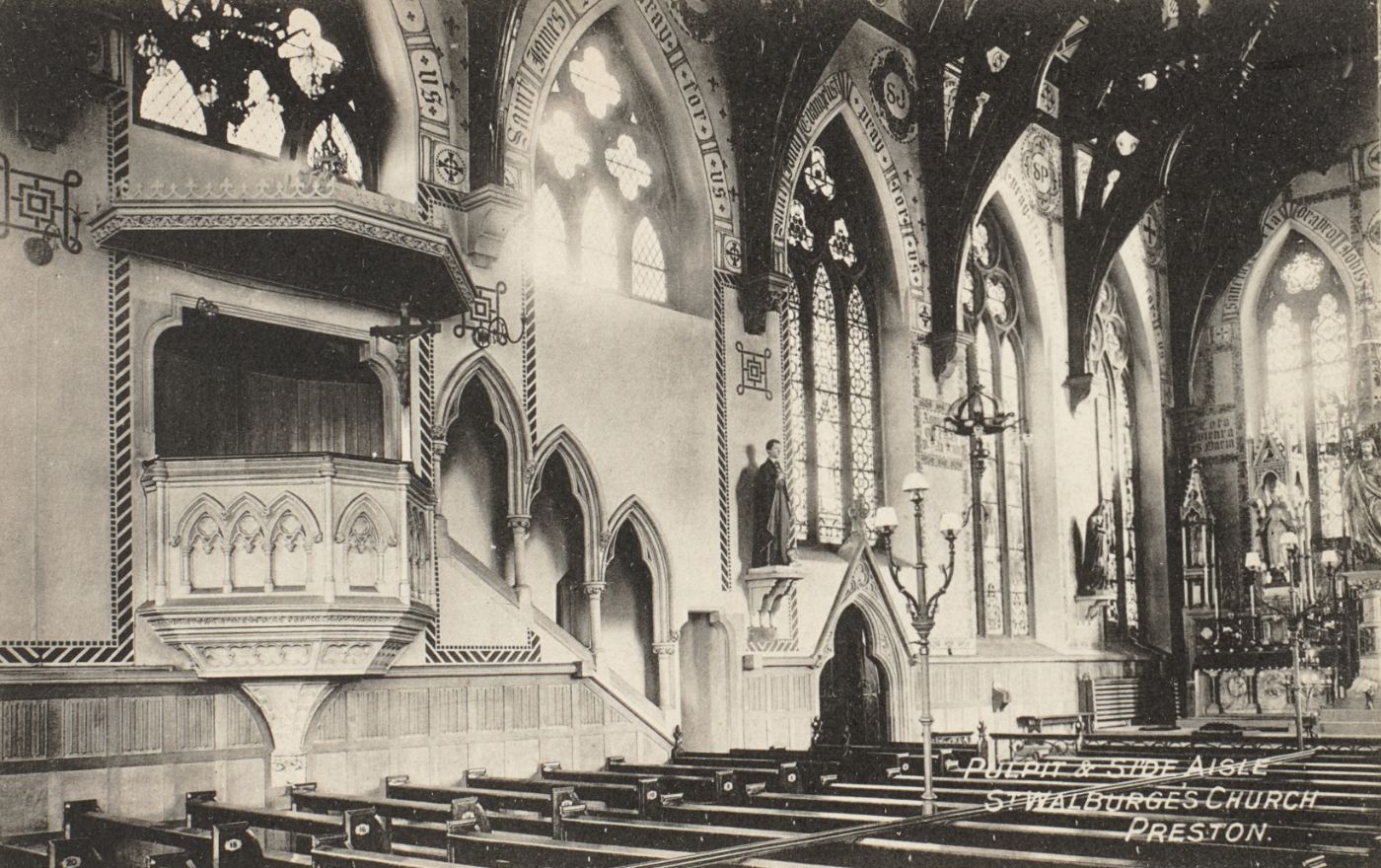 Printed postcard of the pulpit and side aisle at St Walburge's, painted texts and stained glass along the wall arcade, pews in the foreground, captioned "Pulpit & Side Aisle, St Walburge's Church, Preston.