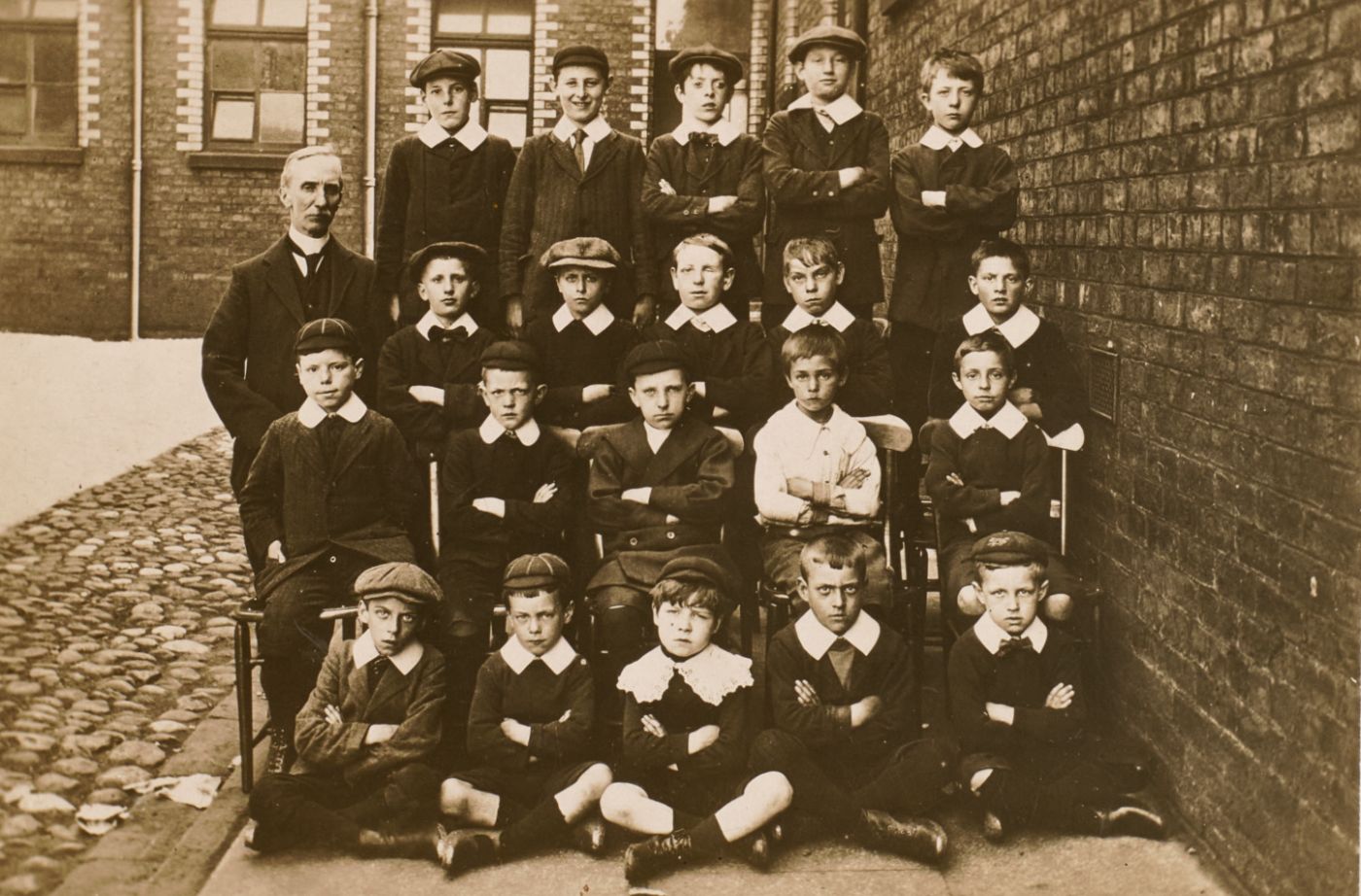 Boys in caps and collars arranged in rows for a school photograph, schoolmaster standing to one side.