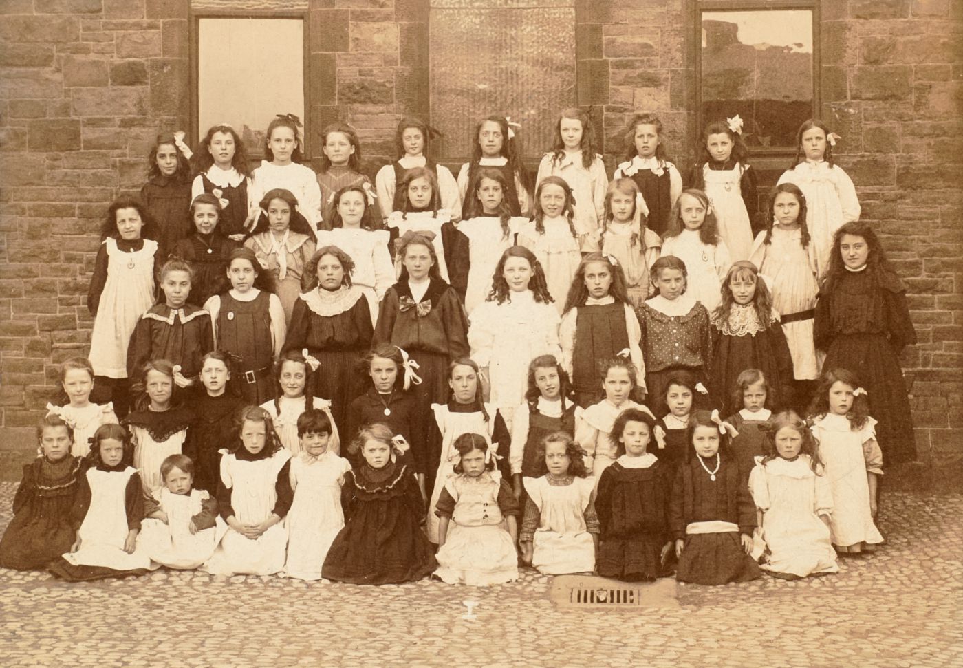Girls of Talbot School posed in four rows outside the school building, pale pinafores over dark dresses, hair tied with ribbons.